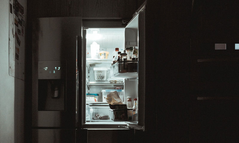 Refrigerator door open with light on in dark kitchen