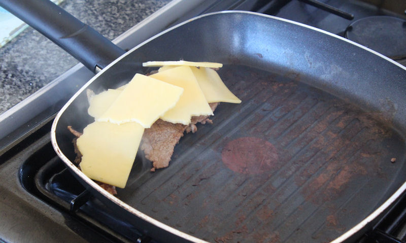 Melting cheese on beef strips in pan