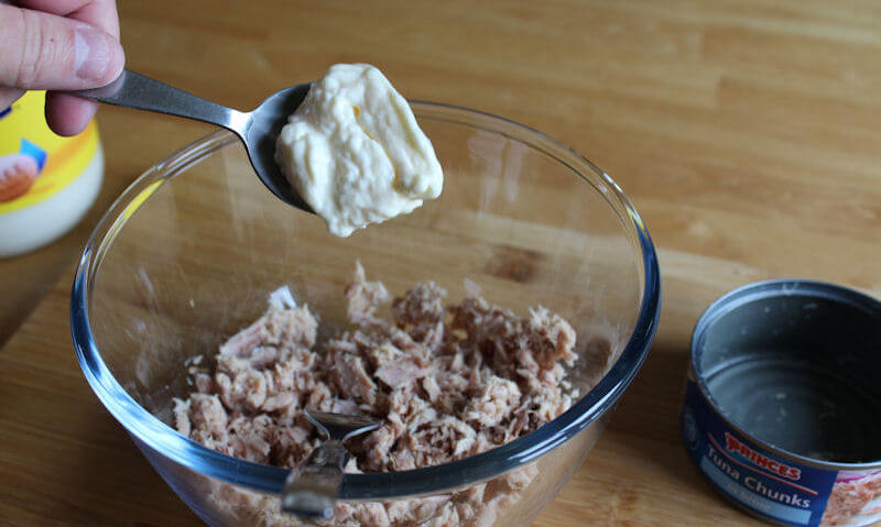 Tablespoon of mayonnnaise being added to dry tuna chunks